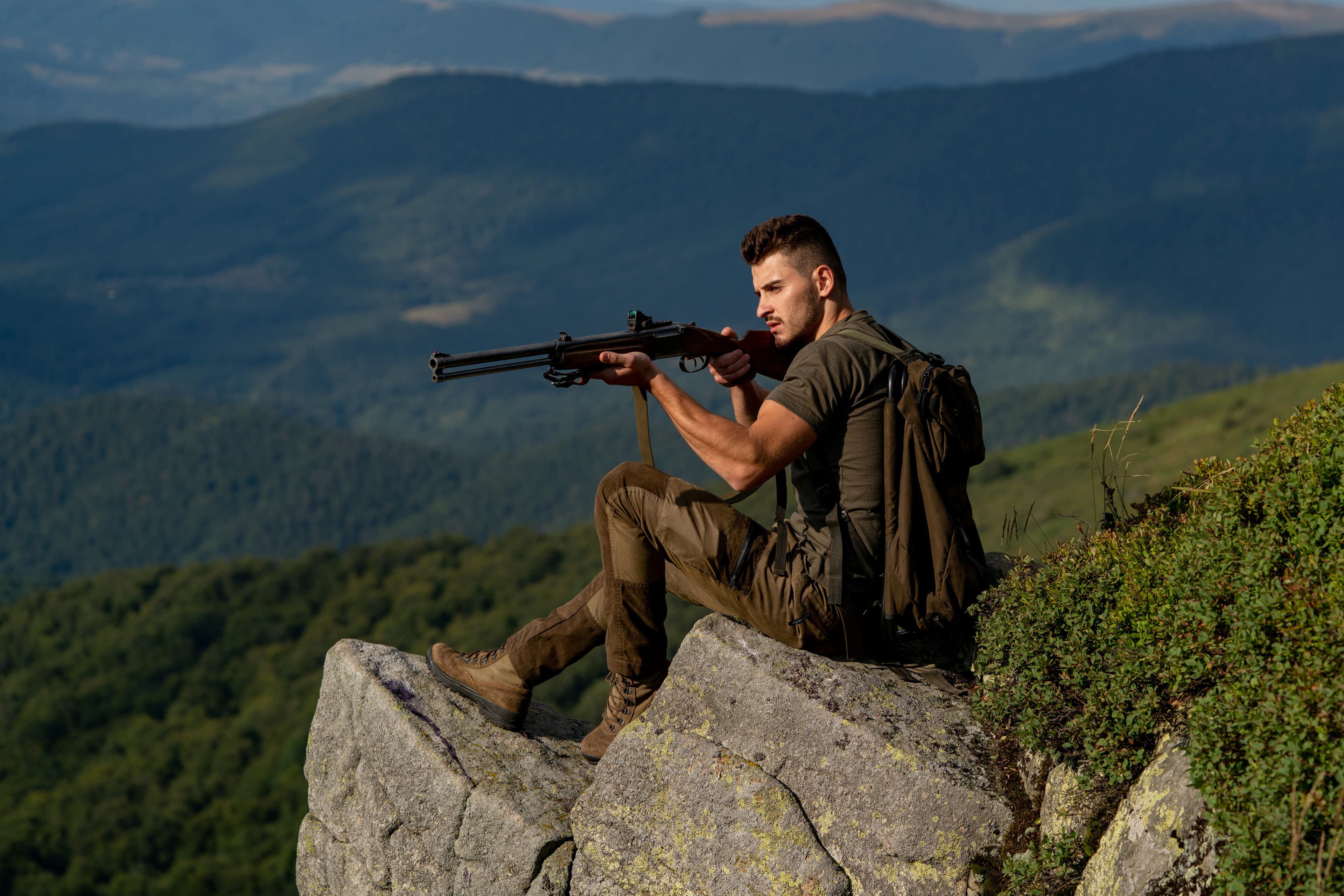 Man outdoors holding a rifle in the mountains