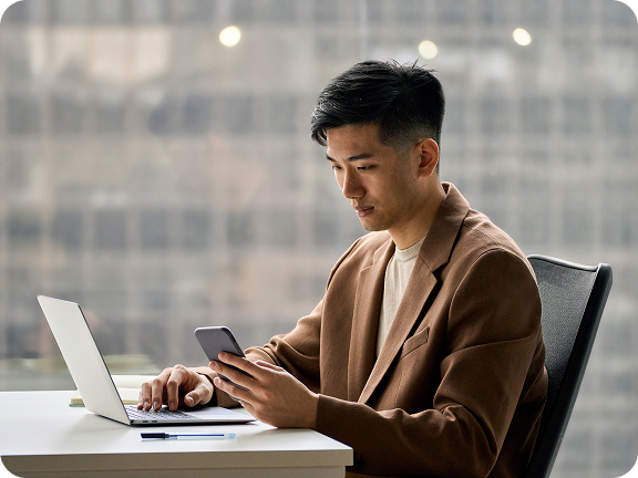 Man sitting in front of laptop holding phone